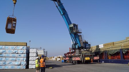 Crane lifting materials in port yard.