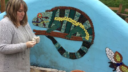 A lady beside a blue wall with a chameleon and butterfly painted on the wall.