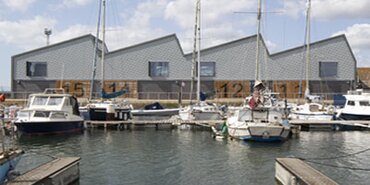 The marina with a grey building opposite, the roof is zig-zagged to appear like waves.