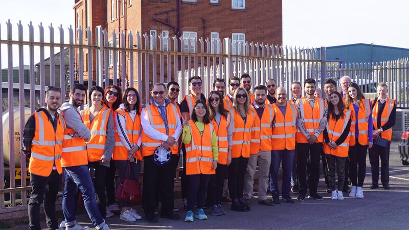A large group of people all wearing orange high vis on a tour of the port.