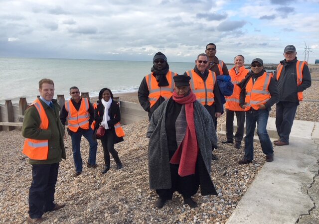 Ten people standing on a stoney beach wearing orange high vis vests.