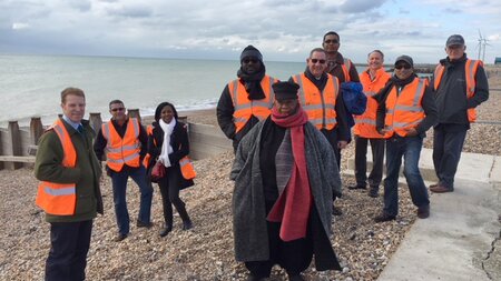 Ten people standing on a stoney beach wearing orange high vis vests.