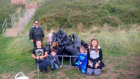Young children sit beside bin bags of collected rubbish on the grass.