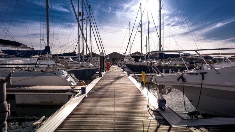 A walkway on a marina, boats are either side with their sails tucked away.