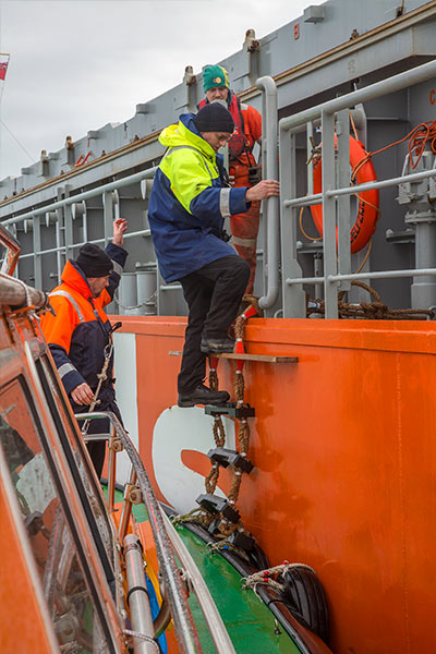 A pilot boarding onto a large orange ship.